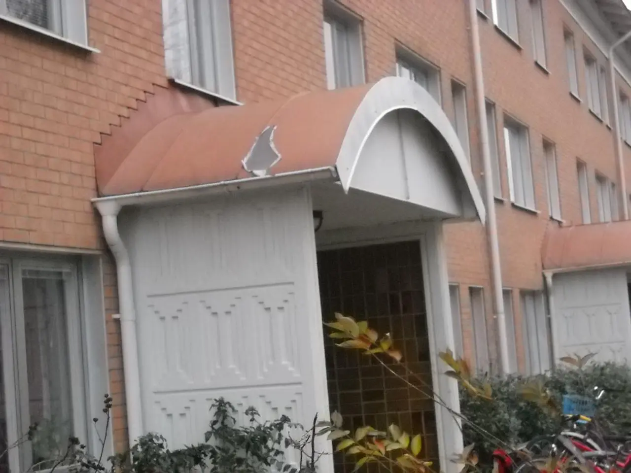 In this image we can see a building and pipes attached to the building and there are few plants and...