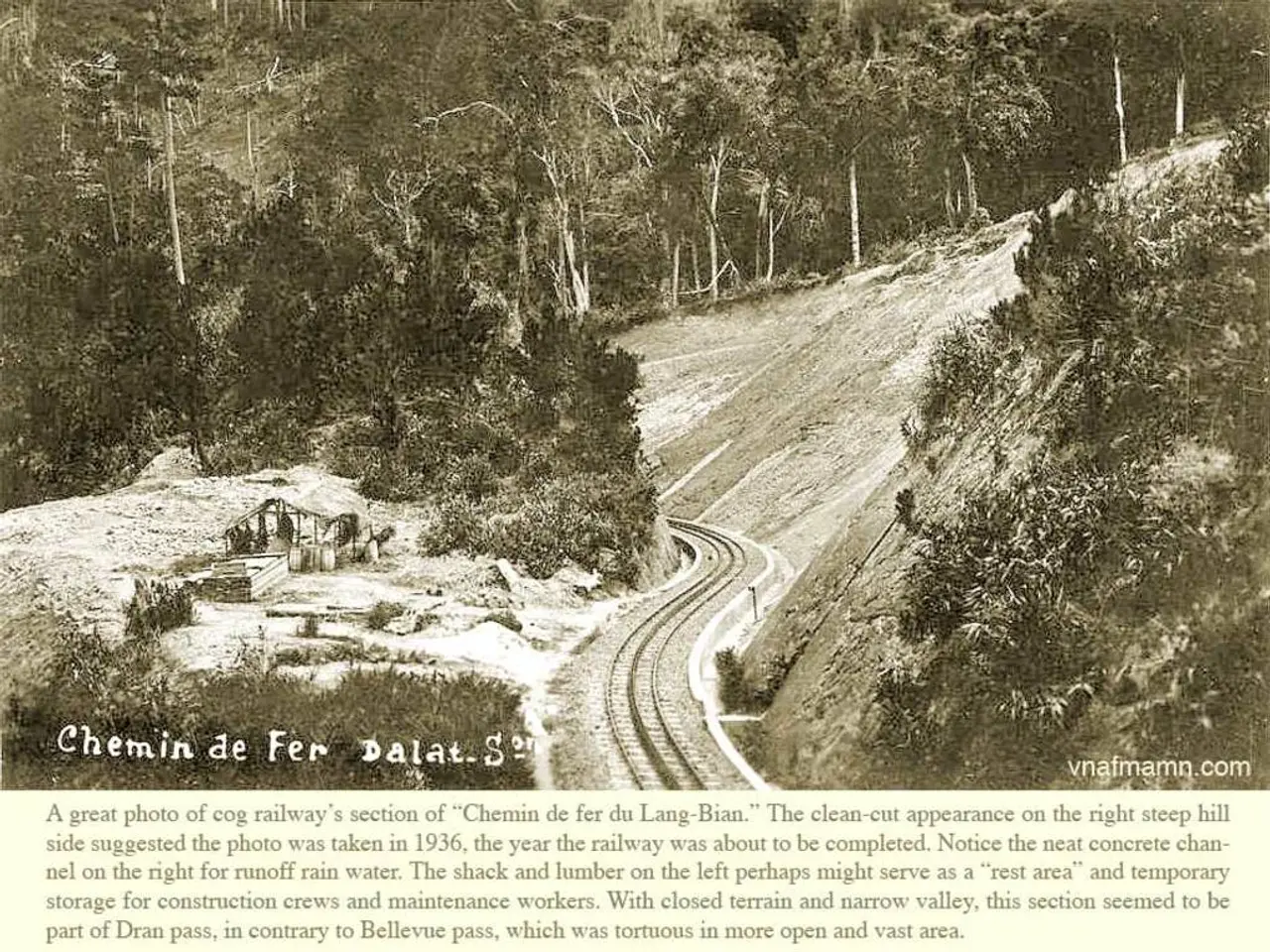 In this image I can see few trees,shed,railway-track and snow. I can see something is written on...