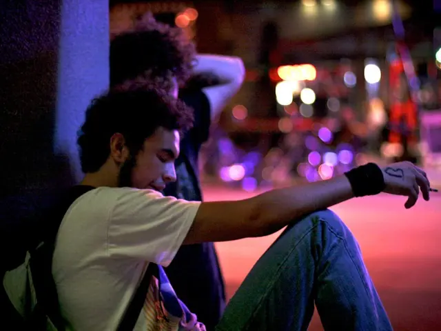 In this image we can see persons sitting on the ground and one of them is holding cigarette and bag...