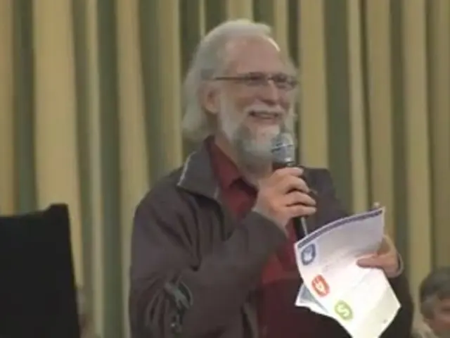 In the center of the image there is a person holding a mic and paper. In the background we can see...