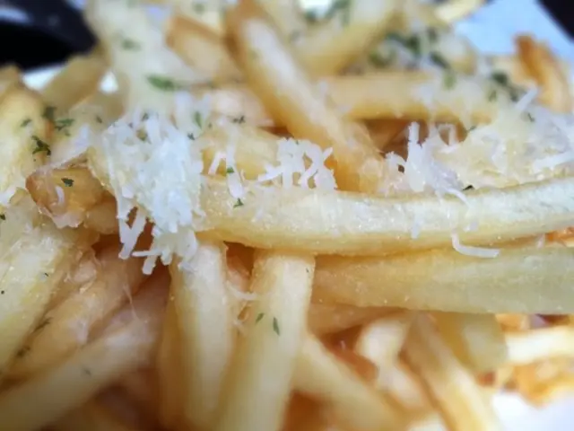 In this image there are so many french fries garnished with cheese.