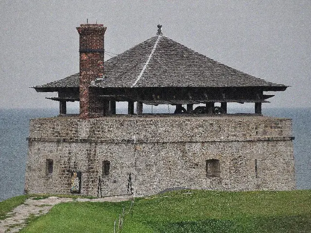 In this image there is a grassland, in the background there is a house and the sea.